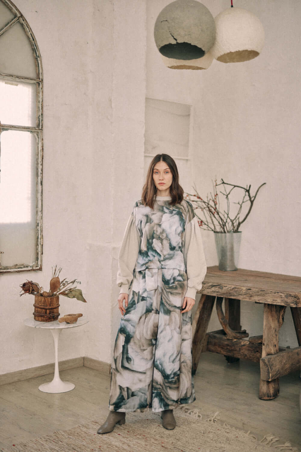 Woman wearing printed wide trousers with autumn design, standing in rustic room with natural decor.