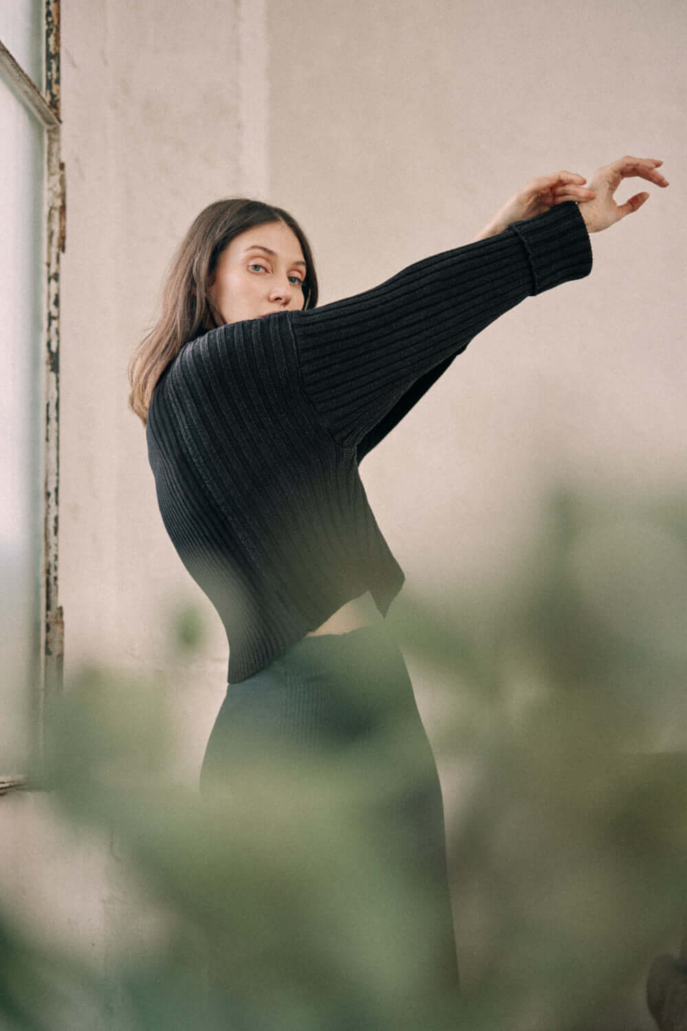 Woman wearing a bicolor black sweater made from organic cotton yarn, showcasing its crop and wide fit with a high neck design.