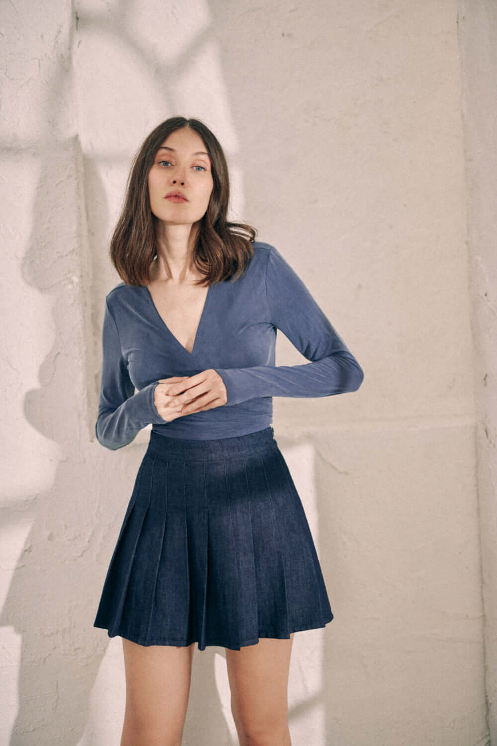 Navy Cupro Wrap Top with Long Sleeves and Thumb Holes, Paired with Denim Skirt, Modeled by Woman in Minimalist Setting