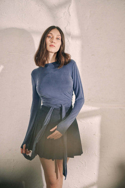 Navy cupro wrap top with thumb holes styled with a black skirt worn by a model against a textured background.