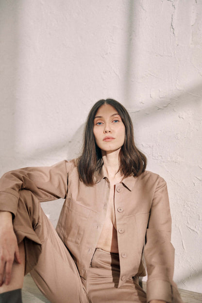 Woman wearing taupe denim jacket with turned sleeves and matching pants, made from organic cotton, featuring COSSAC buttons.