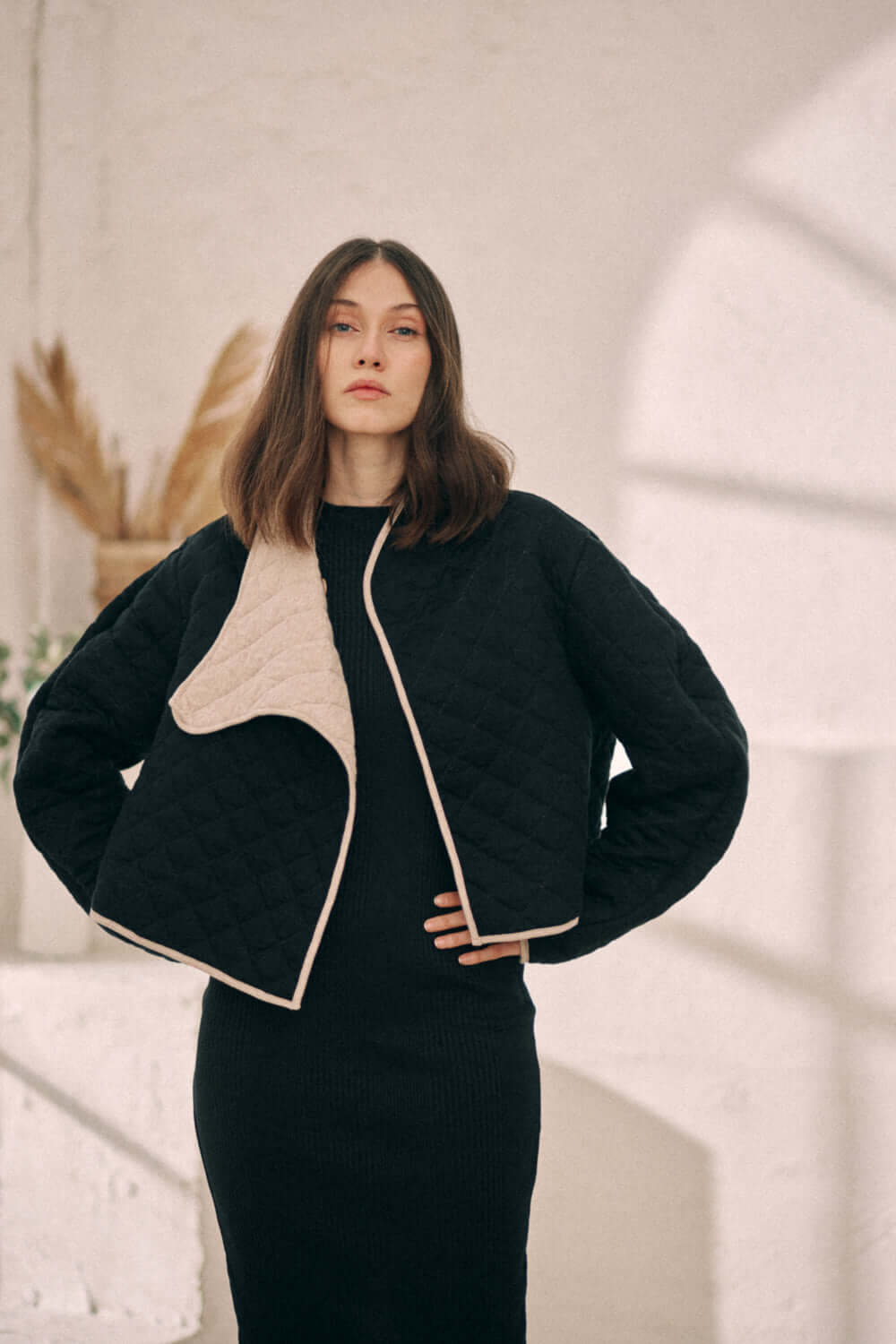 Model wearing black reversible padded jacket with beige lining, crafted from organic cotton and recycled polyester. Sustainable fashion AW24 collection.