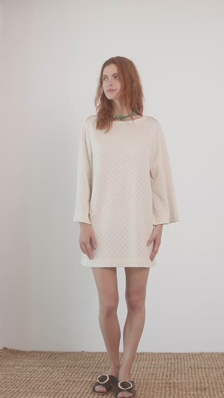 Model wearing an Organic Cotton Crochet Mini Dress with flared sleeves in ecru, showcasing a playful summer style.