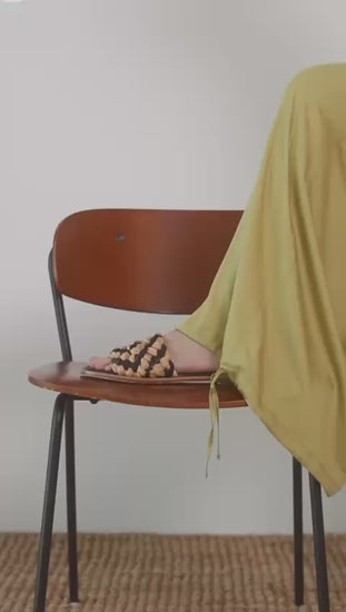 Wide Ecovero Trousers in Soft Olive paired with stylish woven sandals on a wooden chair.