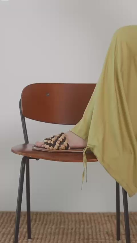 Wide Ecovero Trousers in Soft Olive paired with stylish woven sandals on a wooden chair.