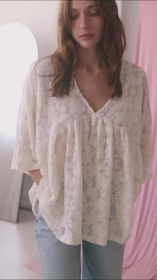 Model wearing an ecru lace boho tunic top with a V-neckline and wide short sleeves, styled casually with jeans.