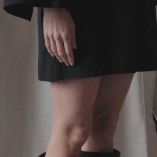 Model wearing a black organic cotton mini dress with flared sleeves and knee-high black boots.
