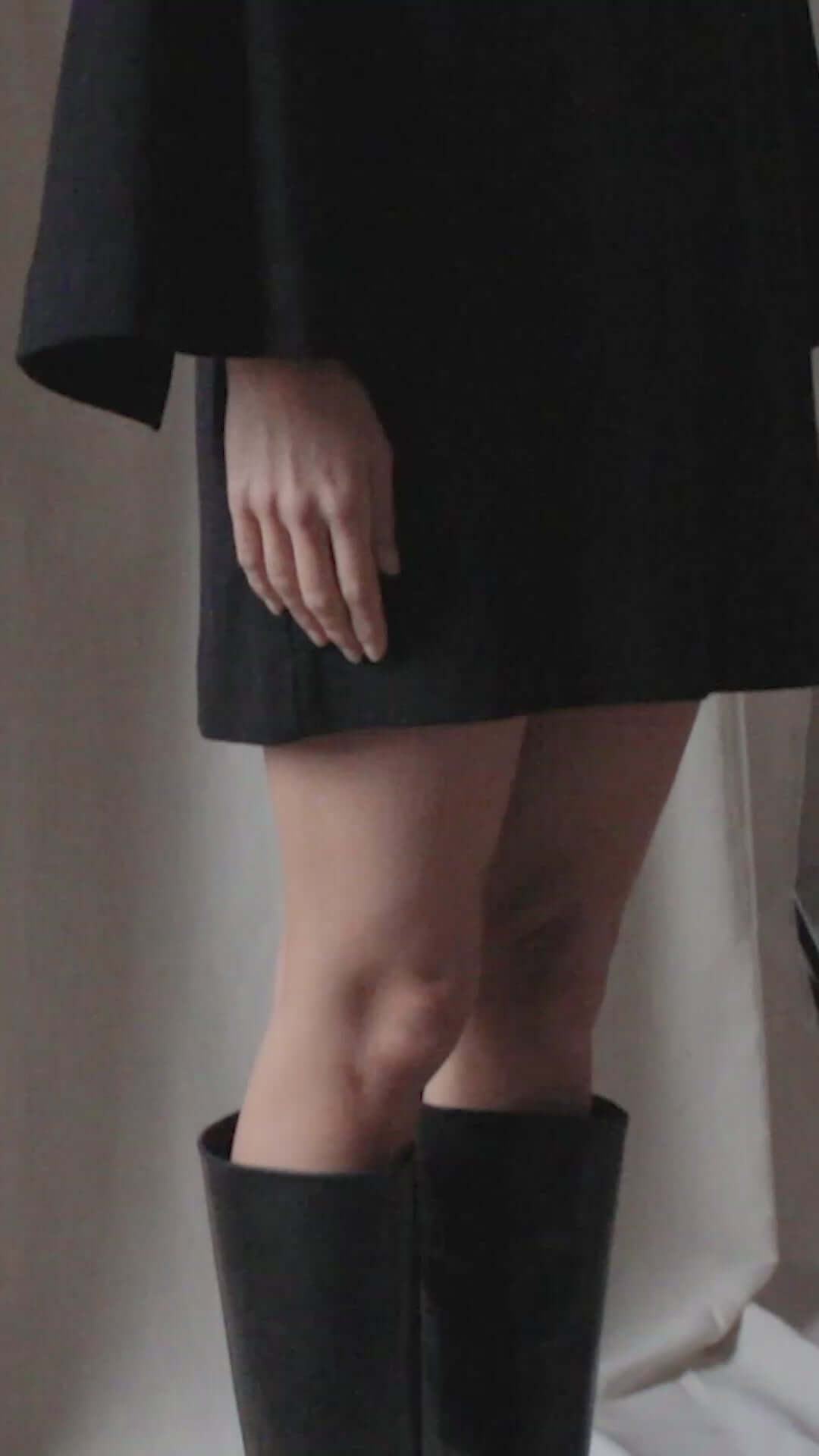 Model wearing a black organic cotton mini dress with flared sleeves and knee-high black boots.