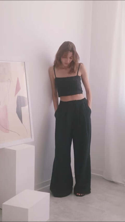 Model wearing a black crop top with adjustable straps and wide trousers, showcasing a stylish and sustainable outfit.
